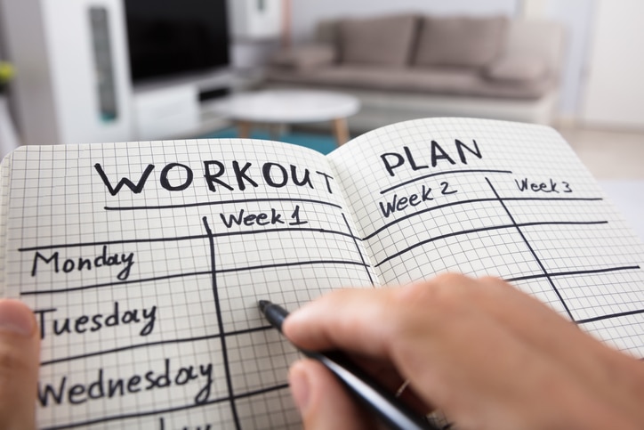 Close-up Of A Person's Hand Writing Workout Plan In Checkered Pattern Notebook