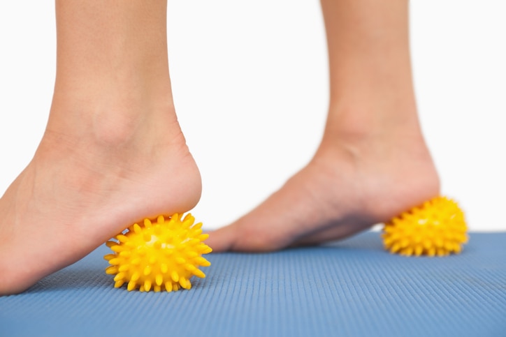 Female feet touching yellow massage ball standing on blue ground