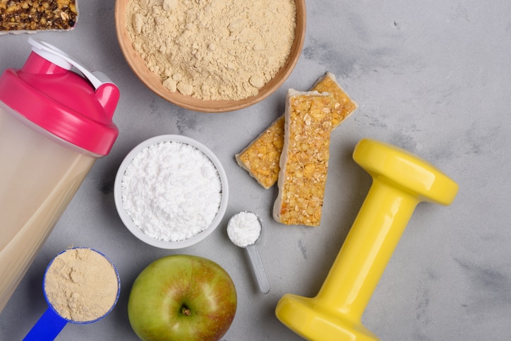 Sport nutrition with vegetarian protein powder and creatine with snacks and dumbbell on concrete background top view flat lay