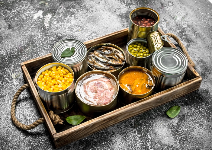 Various canned products in tin cans on a wooden tray. On a rustic background.