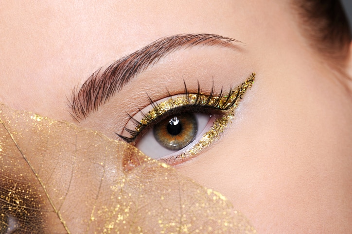 Macro shot of beauty female eye with golden eyeliner make-up covered artificial yellow leaf