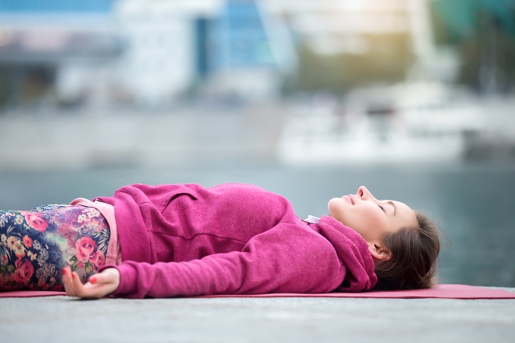 Young attractive woman practicing yoga, lying in Dead Body exercise, Savasana, Corpse pose, relaxing, refreshing after sport, wearing nice pink sportswear, outdoor city, river background, close up