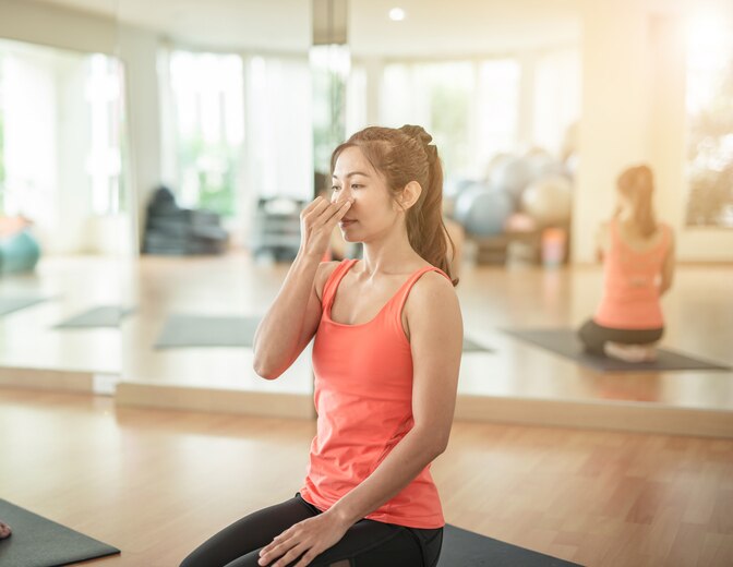 woman yogi practicing yoga, sitting in Padmasana, Lotus pose, using Alternate Nostril Breathing, nadi shodhana pranayama, working out,in yoga studio