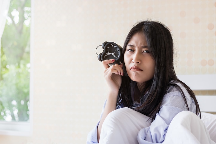 Asian girl looking alarm clock after waking up late.