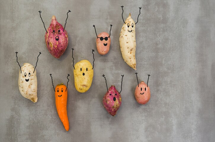 Great concept of healthy eating, vegetables with happy faces with arms up, potato, sweet potato, carrot. Gray background, polished concrete.