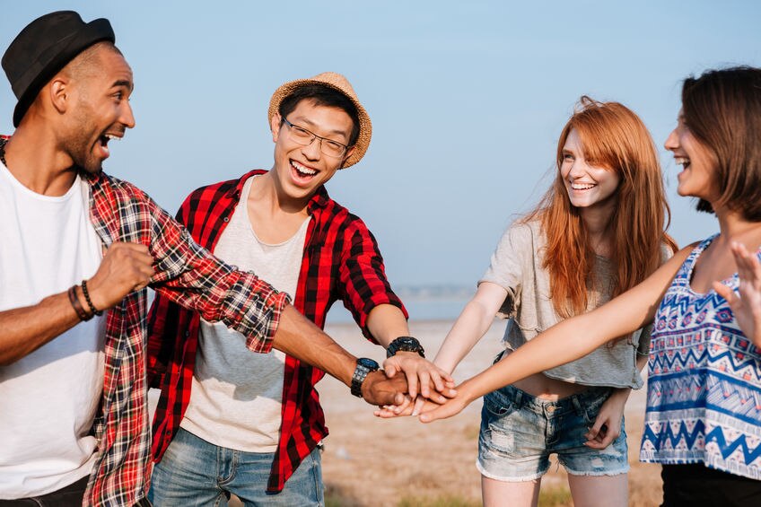 Multiethnic group of cheerful young friends standing and joining hands outdoors