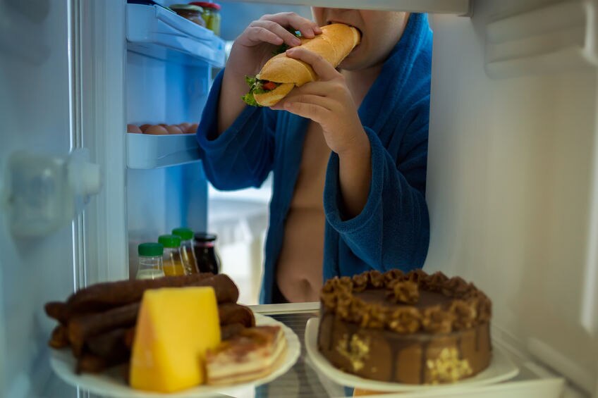 At night corpulent man violates diet with big sandwich roll