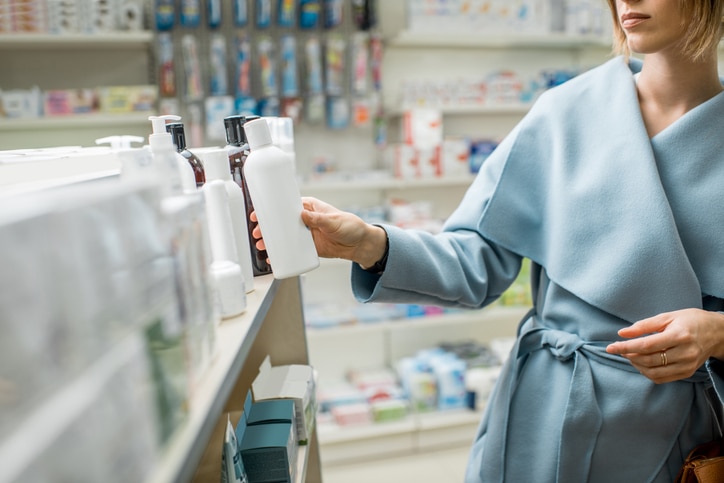 Woman taking a bottle with cosmetics from the shelf of the pharmacy supermarket