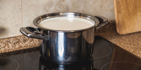 Boil milk. Metal pan with milk stands on a modern black electric stove