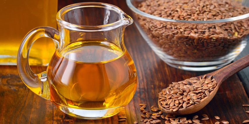 Brown flax seeds on spoon and flaxseed oil in glass jug on wooden table. Flax oil is rich in omega-3 fatty acid.