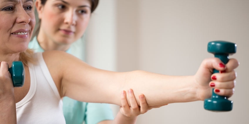 Woman exercising with dumbbells insured by physiotherapist