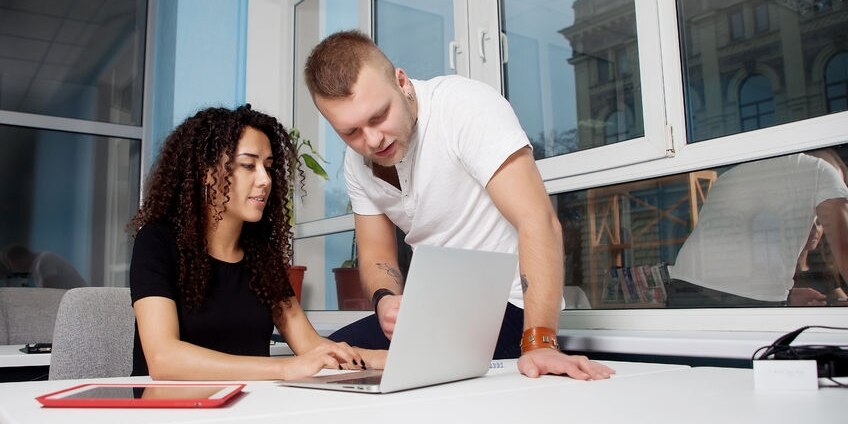 51522816 - business partner sitting at his wooden white table in front of his computer in a luminous white office with large windows. heshowing a graphic on the screen  brunette female, male sitting on a table